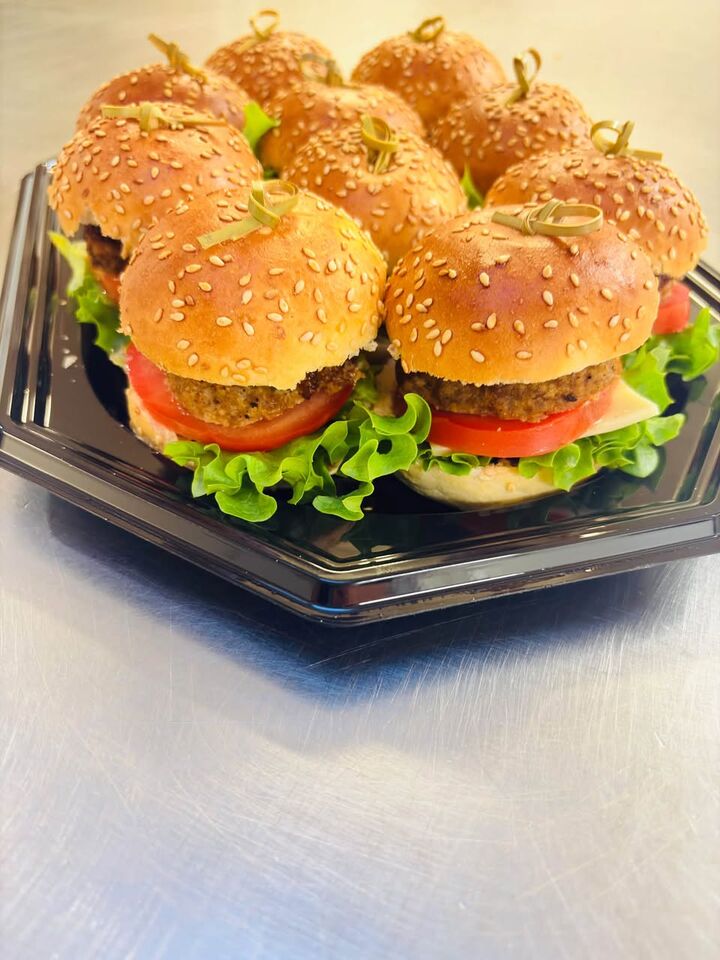 Miniburgers met sesambroodjes, sla en tomaat op een zwarte schotel, van Catering bij Natalia.