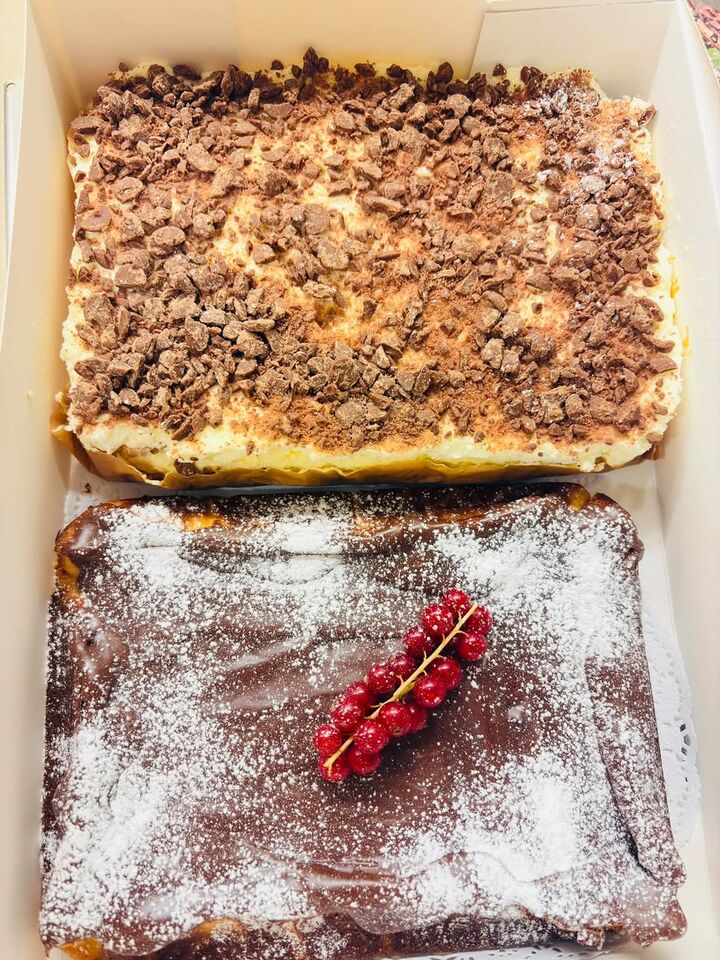 Twee taarten van Catering bij Natalia in een doos: een met chocoladeschilfers, een met poedersuiker en rode bessen.